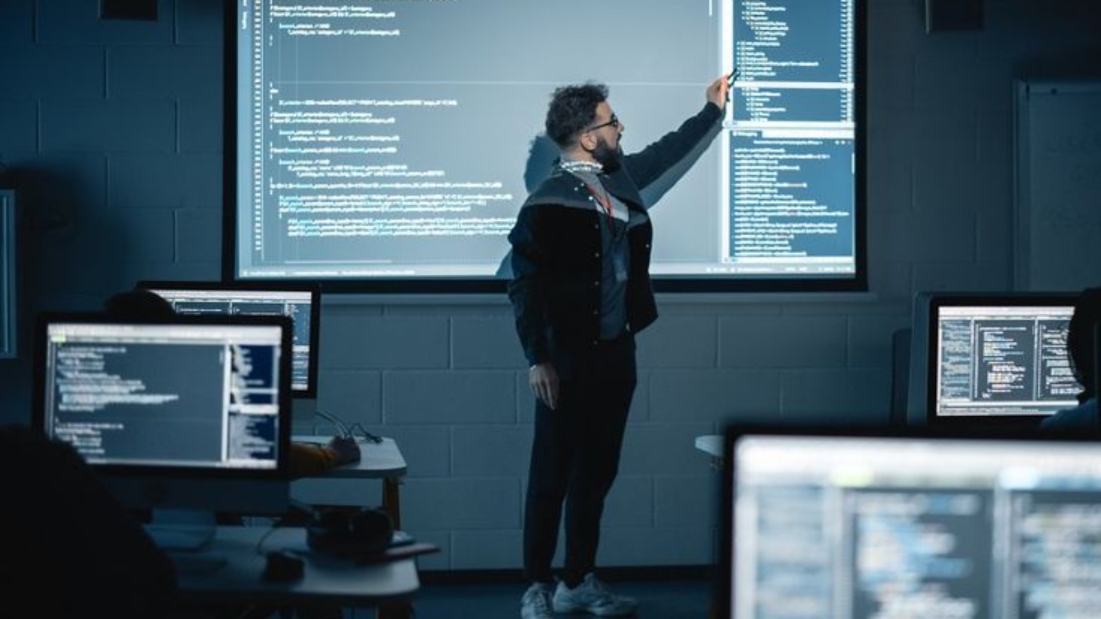 Teacher Giving Computer Science Lecture to Diverse Multiethnic Group of Female and Male Students in Dark College Room_ Projecting Slideshow with Programming Code. Explaining Information Technology (1)